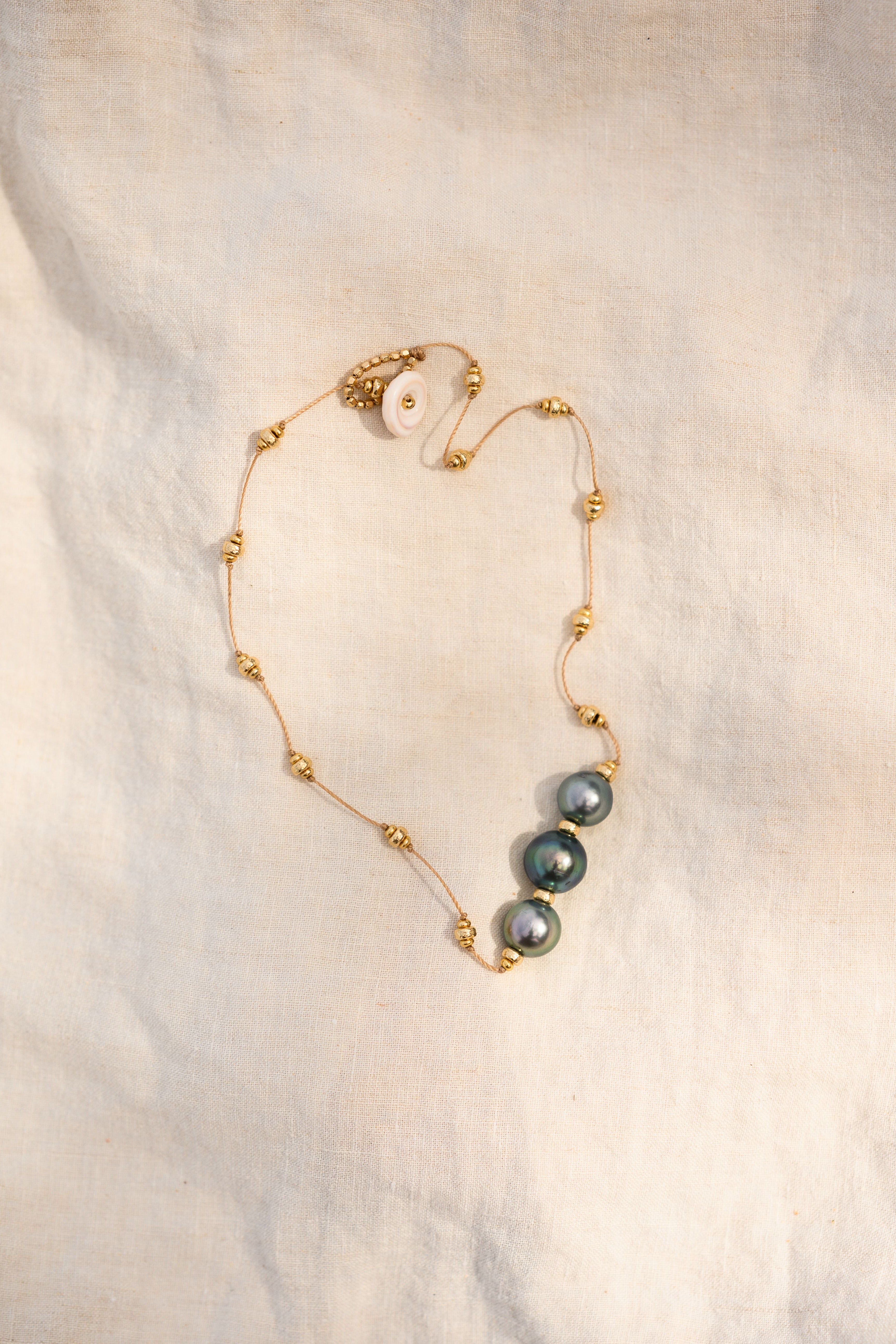 Gold necklace with three dark pearls on a textured beige background