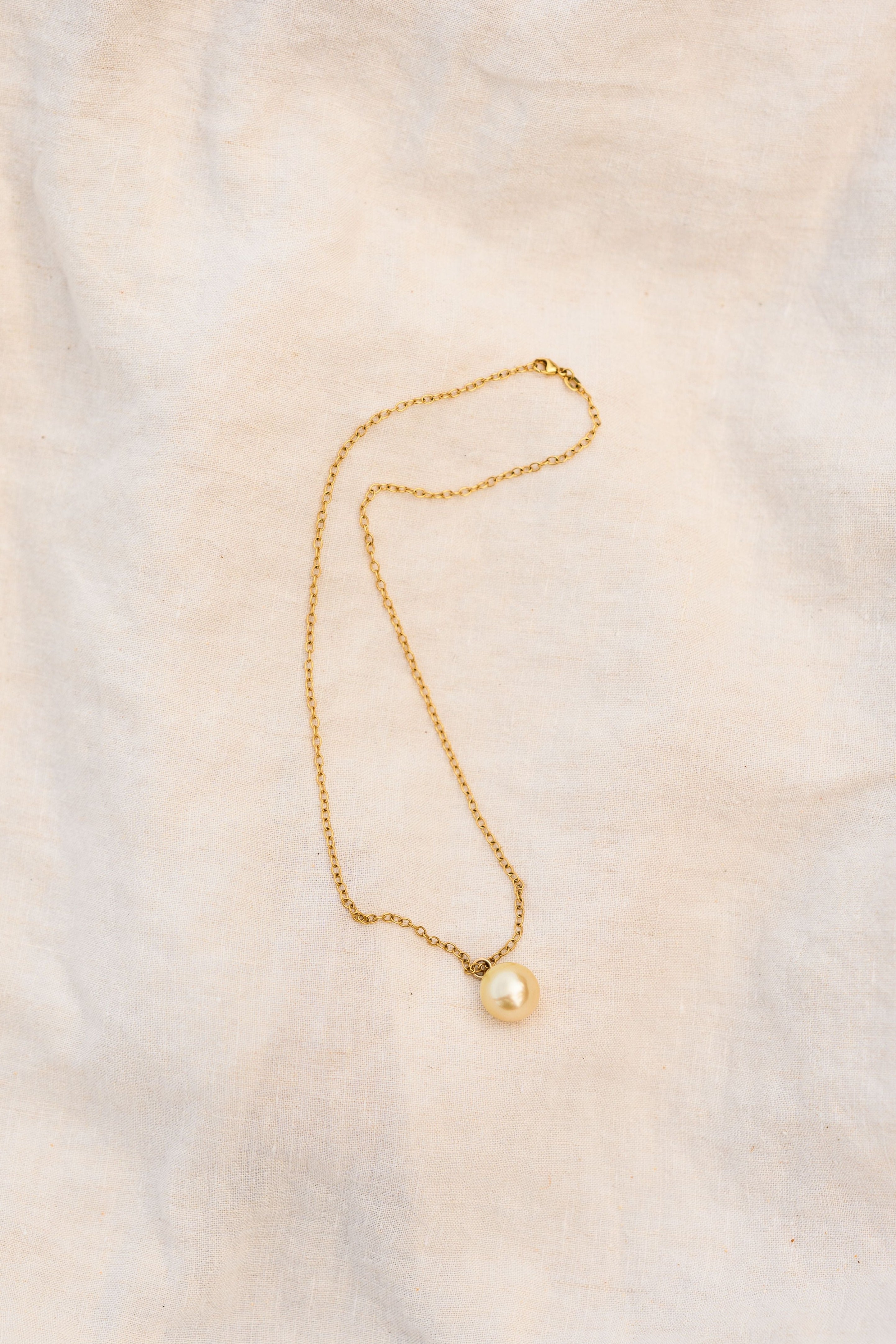 Gold necklace with a single pearl on a soft beige fabric background
